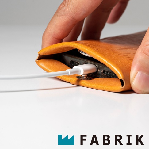 FABRIK 商標旁，橙色皮革手機套內，一個 iPhone 正在充電，充電線連接到手機。