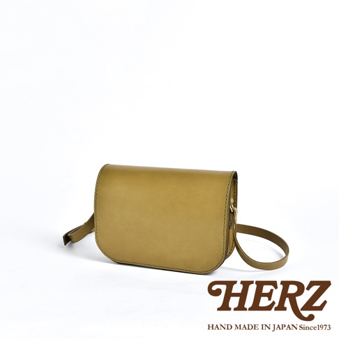 職人手作皮革翻蓋橫式單肩包，淺褐色，圓潤的翻蓋設計，簡約的縫線，配有一條可調節的皮革肩帶，整體呈現自然的皮革質感。