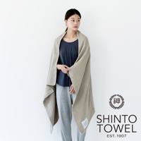 一位女性身披淺棕色2.5層紗浴巾，浴巾材質輕柔，邊緣有縫線，左下方有產品標籤。