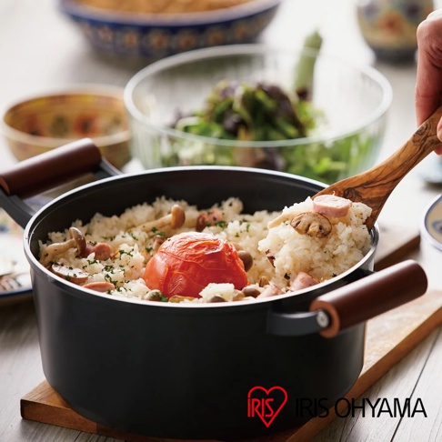 黑色不沾鍋中盛有飯、香菇、番茄和香腸，旁有木質鍋鏟盛起部分飯菜，鍋具兩側有木紋把手。
