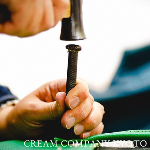 京都職人以槌子敲擊皮革上的銅釦，展現手工製作的細緻工藝。