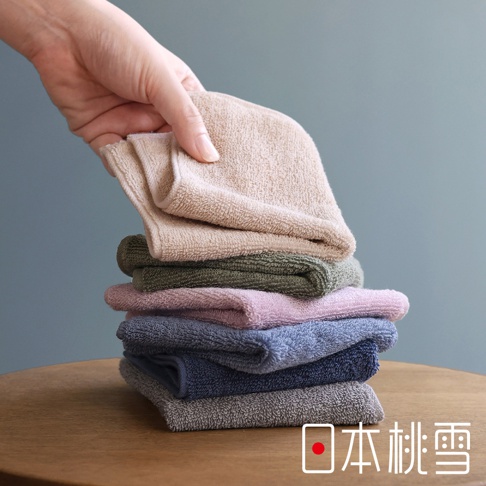 日本桃雪標誌旁的飯店迷你手帕堆疊，由左上方的手正在拿起最上方的淡褐色手帕。