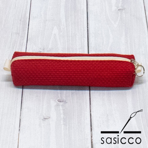 紅色三河木綿刺子織筆袋，帶有米白色拉鍊和掛環，置於淺色木紋背景上。