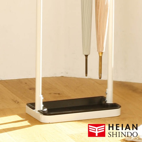 白色直立吊掛傘架，底部為黑色長方形集水盤，架身由白色金屬製成，吊掛著兩把分別為米白色與淺粉色的摺疊傘。