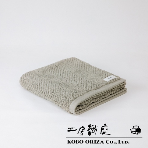ECOR 天然系人字紋有機棉浴巾，呈現淺米色，織有細緻人字紋理，觸感柔軟，邊緣有同色系滾邊，並帶有白色品牌標籤。