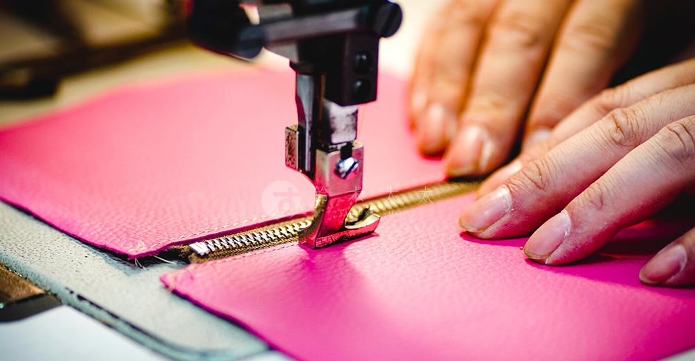 職人正在使用縫紉機縫製桃紅色皮革側背包的拉鍊。
