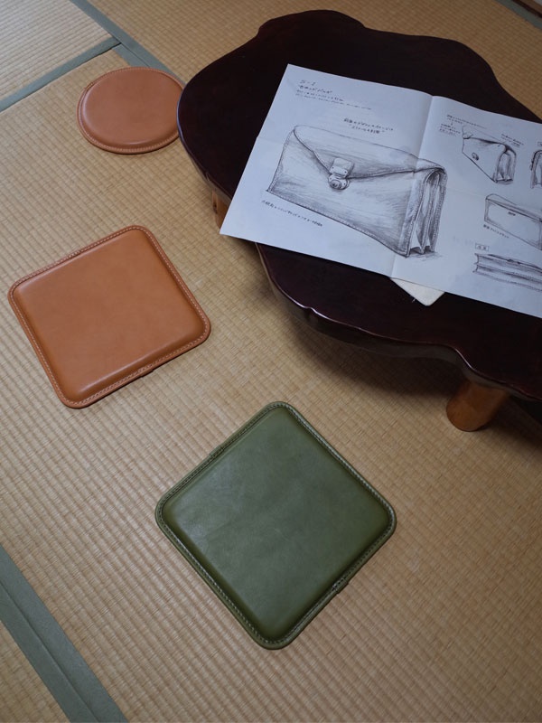 職人手作皮革方形坐墊，一個為棕褐色，一個為軍綠色，兩款皆為方形，邊緣有縫線裝飾。