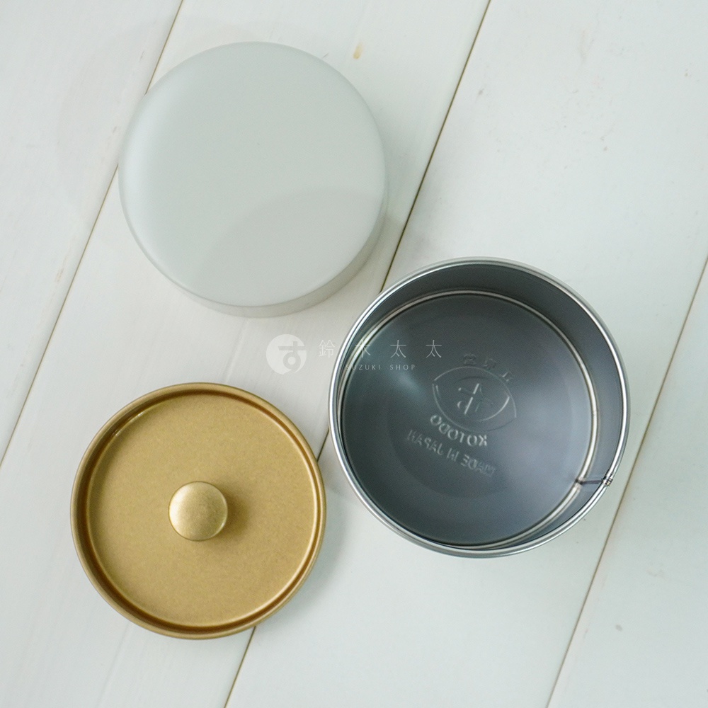 銀色圓形錫製茶葉罐的蓋子、金色帶有圓形提鈕的罐身，以及內部為深灰色的錫製罐體，均呈現簡約設計。