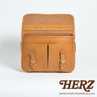 天然皮革製成的淺棕色兩用單肩包，正面有兩個帶有銅釦和皮帶的隔層，翻蓋內有三個黃銅鉚釘。