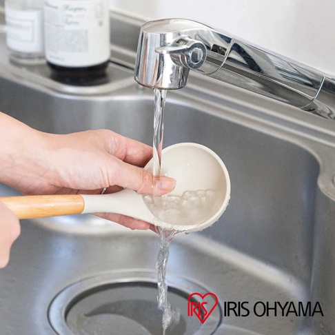 淺米色湯勺，搭配木質手柄，正在水槽下沖洗。