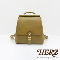 一款橄欖綠的皮革後背包，具有屋瓦造型的翻蓋設計，配有金色金屬扣環和皮革揹帶，展現職人手作質感。