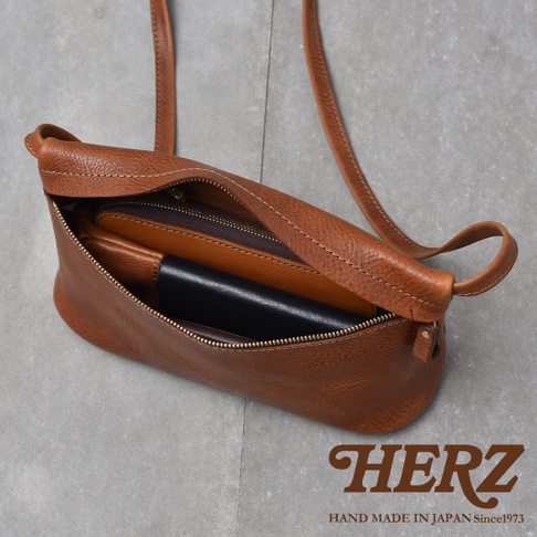 一個棕褐色的皮革斜背包，裡面裝著一個錢包和一個黑色皮夾，包包敞開著，露出拉鍊內袋。