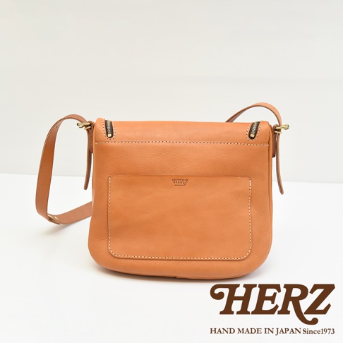 HERZ 品牌職人手作棕色皮革大容量馬鞍包，正面有一個方形外袋，側邊有拉鍊細節。
