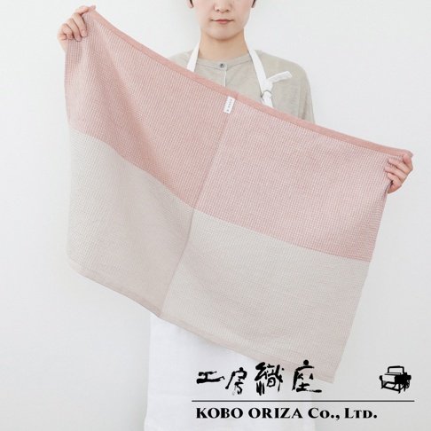 一位女子手持一條粉色與米色拼接的 WAFLE 棉麻混紡拭巾，拭巾有著鬆餅般的立體紋理，左側印有 KOBO ORIZA Co., LTD. 字樣。