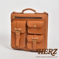 棕色皮革三口袋三用後背包，正面有兩個帶有銅扣和皮帶的貼袋，上方有一個拉鍊袋和一個提把，整體設計簡潔大方，材質為天然皮革。