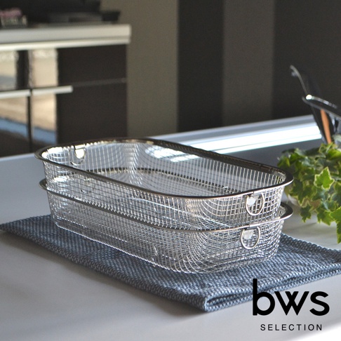 兩只銀色不鏽鋼網狀淺型瀝水籃堆疊在灰色織物上，籃子帶有圓形提把，背景為廚房檯面。