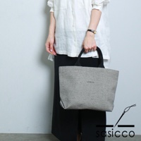 一位女士手提一個經典托特包，包身採用黑白格紋的刺子織布料，配有黑色提把。