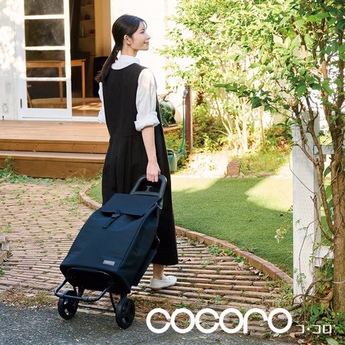 一位女士正在拉著一個黑色輕量折疊大容量購物車，購物車有兩個輪子，上面有一個提把和翻蓋。