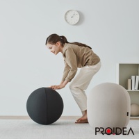 一個小女孩彎腰用雙手觸碰一個深灰色針織圓形平衡球。她右側有一個淺米色針織橢圓形收納椅。