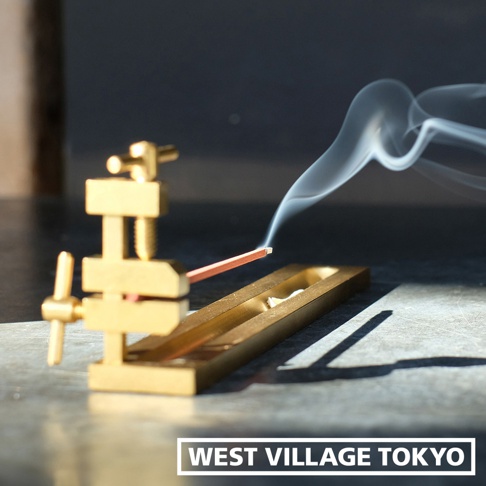 黃銅夾式水平線香架，帶有煙霧繚繞的細長線香，置於金屬托盤中，背景為深色。