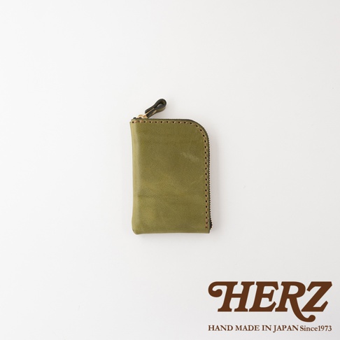 這款日本HERZ手工製作的綠色Stare皮革迷你零錢包，呈現直式收納設計，側面配有拉鍊與皮革拉環，表面質感細膩，右下角印有品牌標誌及手工製作資訊。