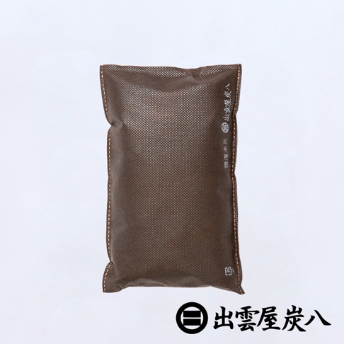 一個深褐色的長方形除濕木炭包，表面帶有細緻的網狀紋理，邊緣有整齊的縫線細節。包裝袋側面印有白色的日文品牌名稱出雲屋炭八與調濕木炭字樣，下方搭配品牌特有的圓形圖示，整體設計簡約實用。