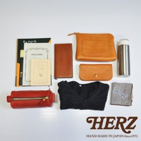 皮革製品組合：紅色皮革筆袋、棕色皮革長夾、淺棕色皮革手拿包、淺棕色皮革化妝包、黑色毛衣、金屬保溫杯、筆記本、雜誌。