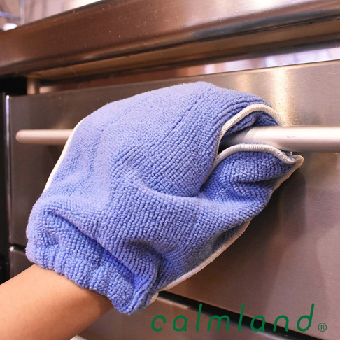 一隻藍色超細纖維清潔手套，手套表面有細小的絨毛，邊緣有白色滾邊，正套在不鏽鋼烤箱的把手上。