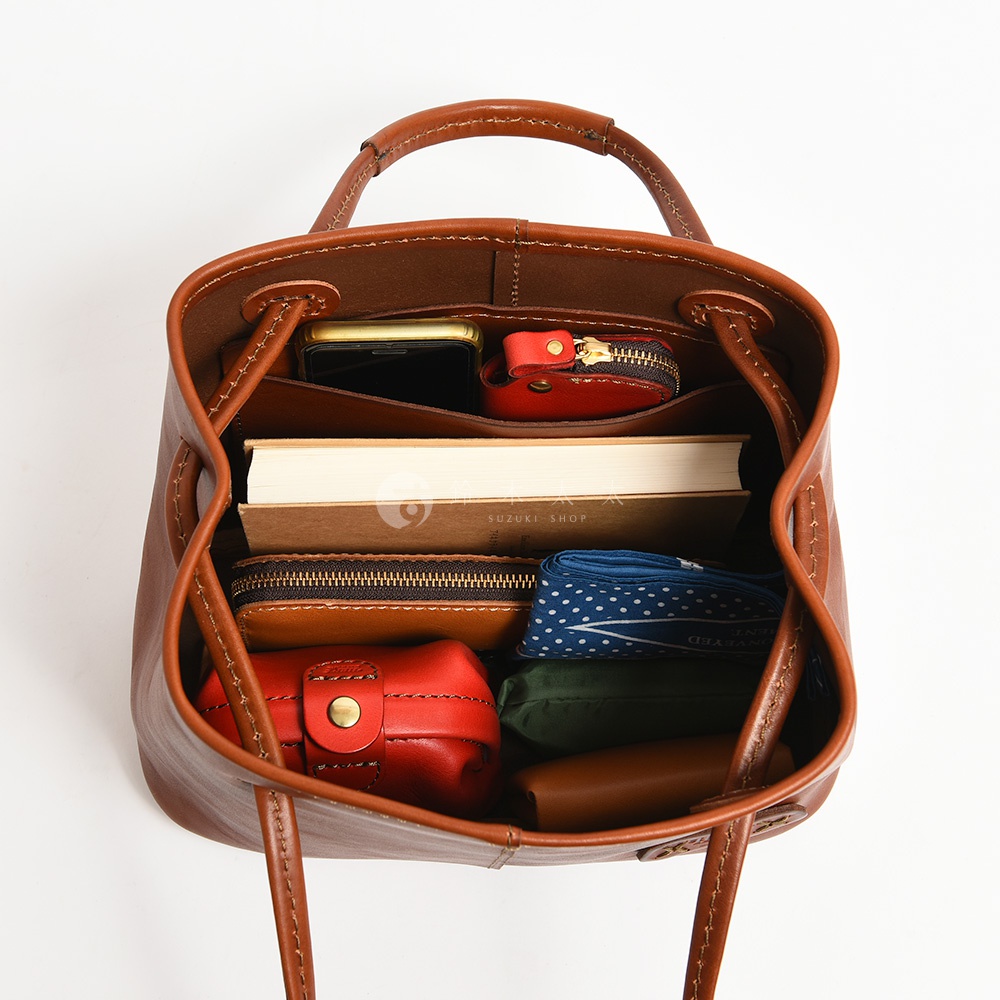 一個棕色皮革托特包，內有手機、書本、錢包、小物包和頭巾。