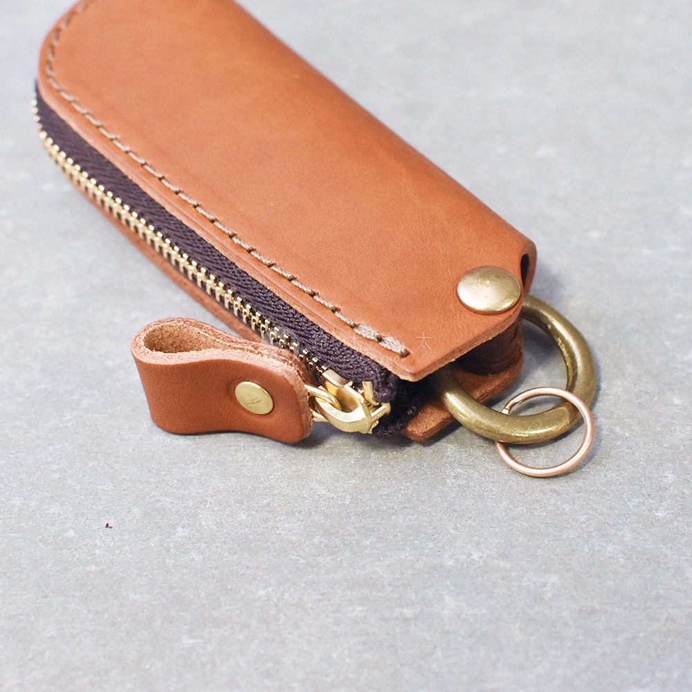 職人手作皮製鑰匙包，採用棕色皮革，搭配黃銅色拉鍊、釦子及掛環。