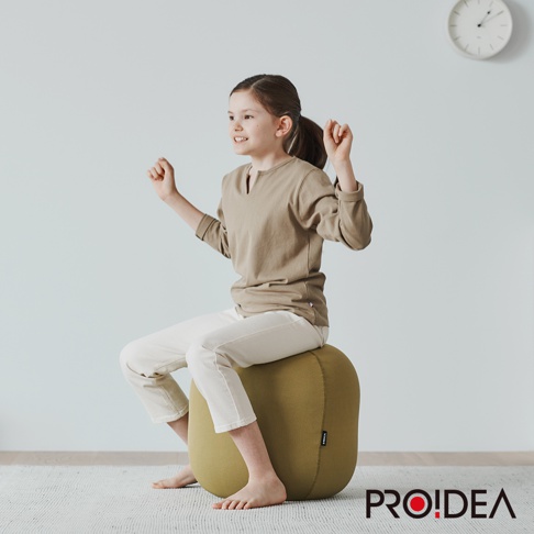 一位女孩坐在橄欖綠色針織彈力平衡球上，該平衡球為迷你款，球體材質為針織，表面有細緻紋理。