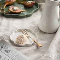 白色花型陶瓷甜點盤，盤面帶有細緻紋理，盤緣為波浪形狀，盤上放置一個淺粉色蛋白霜甜點和一支金色叉子。