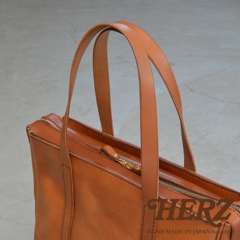 職人手作的棕色皮革肩背拉鍊托特包，包身線條簡潔，搭配金屬拉鍊與手挽帶，展現經典質感。