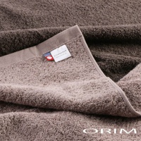 兩條深棕色和淺棕色的今治毛巾，柔軟蓬鬆的毛圈材質，其中一條毛巾的邊緣縫有印有 ORIM 品牌標誌和網址的白色標籤，標籤旁還有藍、白、紅三色條紋裝飾。