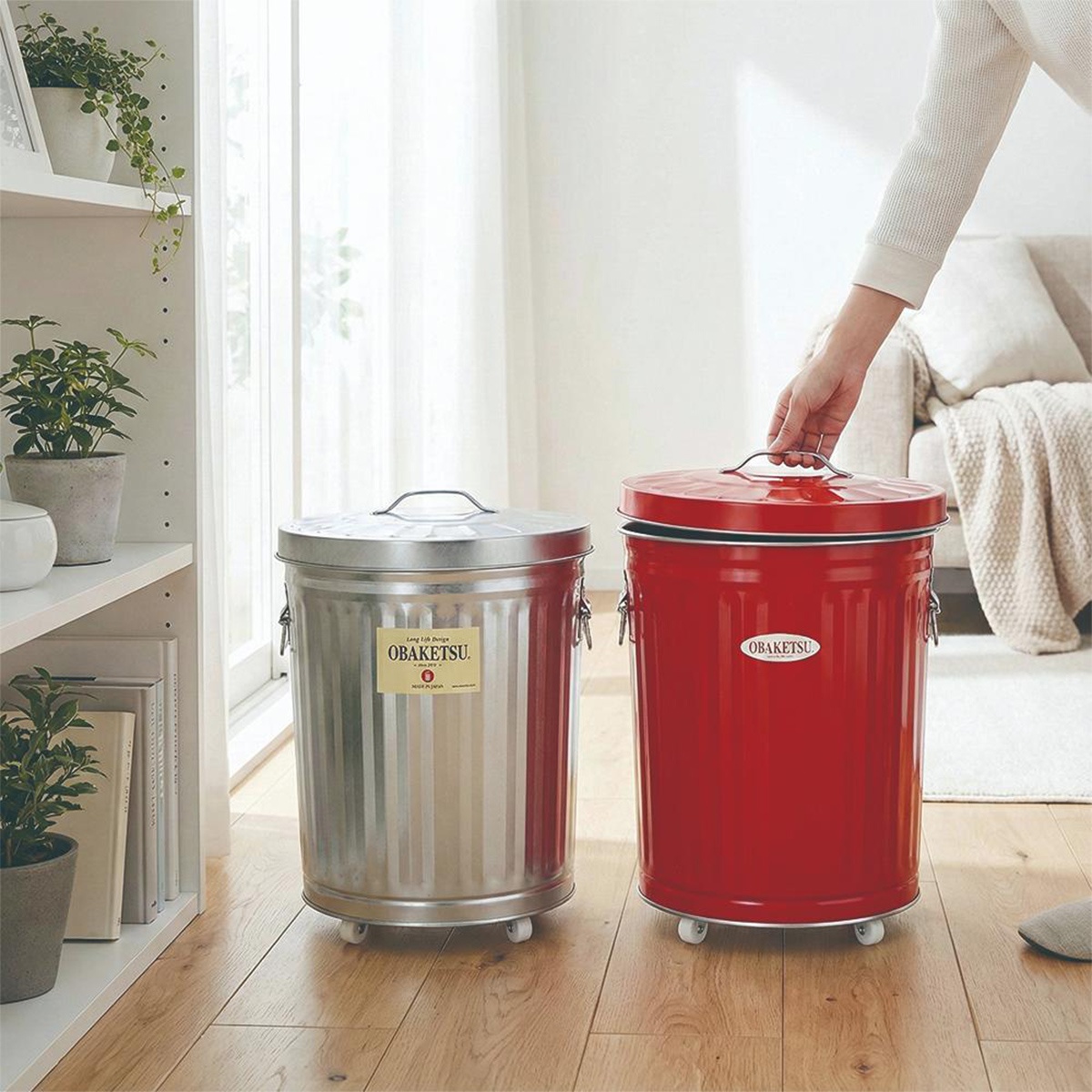附輪 OBAKETSU 鍍鋅鋼製垃圾桶，一個銀色，一個紅色，放在木地板上。