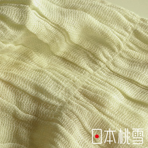 這是一張日本桃雪品牌的四季萬用抗UV純棉紗布圍巾特寫，展現了細緻且具有自然褶皺感的米白色紗布材質，織紋清晰且柔軟透氣，圖片右下角印有日本桃雪的品牌字樣。