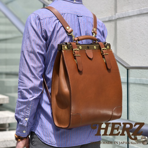 職人手作的復古皮革後背包，主體為棕色牛皮，搭配金屬口金和黃銅色搭扣，設計簡潔，展現皮革質感。