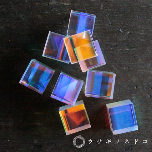 七個透明方形稜鏡立方塊，表面呈現彩虹般的光澤，在深色背景上反射出藍色、紫色、橙色和黃色等色彩。