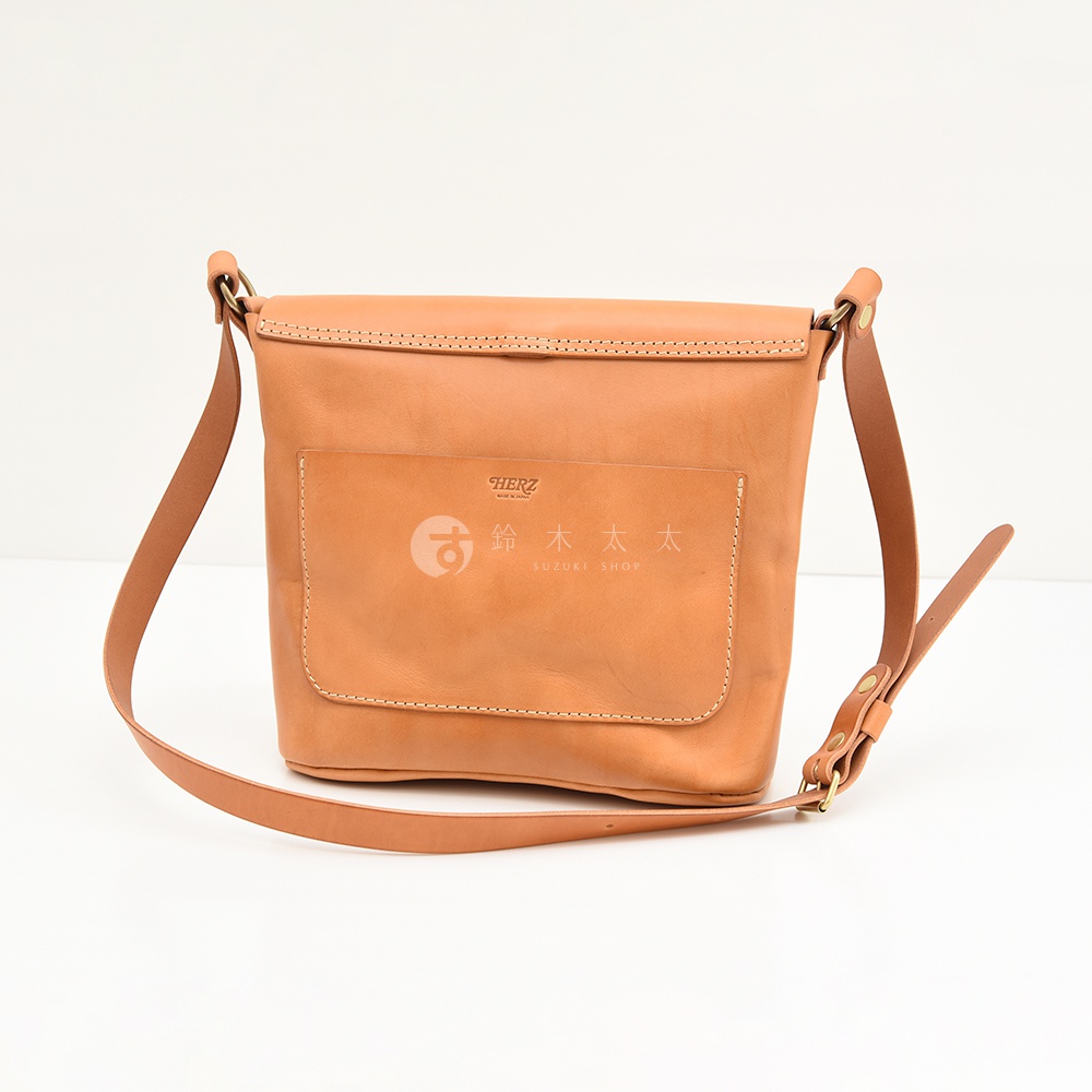 日本HERZ職人手作皮革雙扣旅行郵差包，淺棕色皮革材質，外有一個帶有品牌標誌的方形口袋，整體設計簡約，可作為斜背包使用