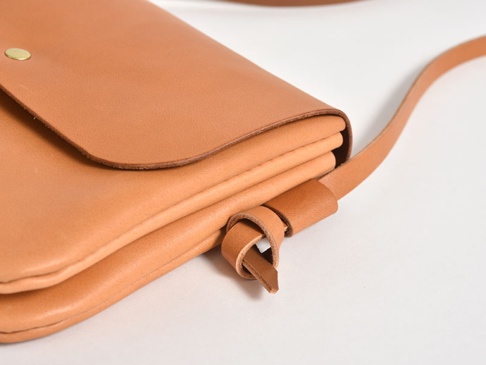 職人手作皮革直式隨行袋 (CP-9)，淺棕色皮革材質，簡約設計，配有金屬按扣及可調節的皮革背帶，皮質細膩，邊緣處理圓潤。