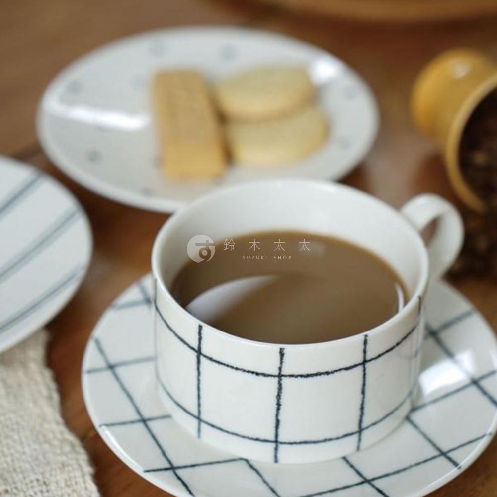 白色陶瓷手繪馬克杯，飾有黑色格紋圖案，搭配同款杯碟，杯中盛有咖啡。
