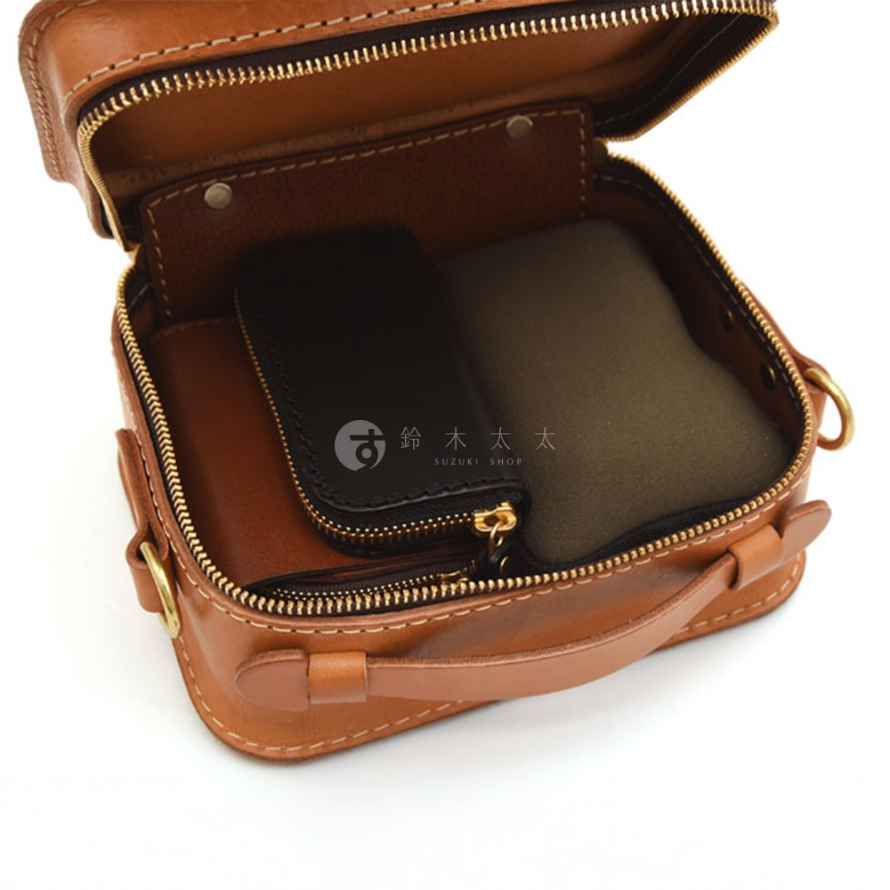 以皮革製作的迷你小方包，打開拉鍊，內部可見黑色小物袋與橄欖綠內襯，包款正面有一個手提把。