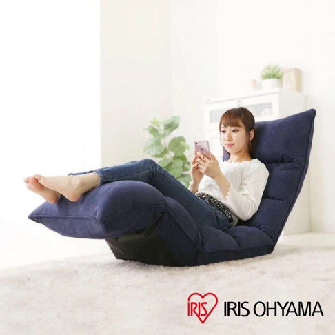 深藍色多段式紓壓單人沙發床，布面材質，附有可調整角度的靠背與腳墊，一位年輕女性正坐在上面使用手機。