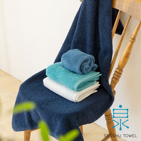深藍色、藍色、青綠色和白色的envelopper迷你浴巾，疊放在木椅上，浴巾質地柔軟，長纖維。