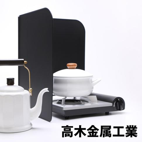 一組黑色的L型折疊擋油板，置於白色背景前，旁邊有一個白色茶壺及一個正在煮食的白色鍋子，鍋子置於一個小型爐具上。