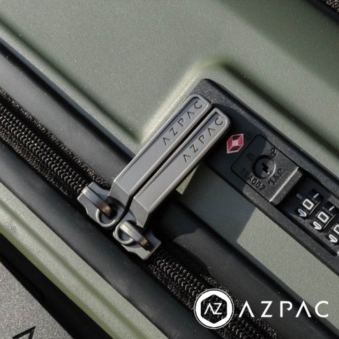 特寫鏡頭拍攝軍綠色的 AZPAC 25 吋前開口煞車行李箱，焦點位於印有品牌標誌的深灰色金屬拉鍊頭，以及側邊嵌入式 TSA007 海關密碼鎖的細節，行李箱外殼呈現平滑的霧面質感。