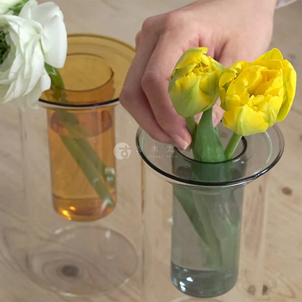 AXCIS PINO 雙層可拆玻璃花瓶-高款，一個裝有白色花朵的琥珀色玻璃花瓶，另一個則由手放入兩朵黃色鬱金香。