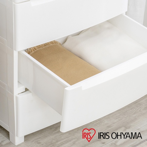 白色塑膠五層抽屜式組合收納櫃，其中一層抽屜內放有卡其色毛毯和白色衣物。