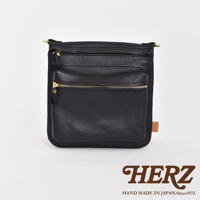 黑色皮革製成的直式斜背包，正面有兩個拉鍊口袋，搭配金色拉鍊和五金。