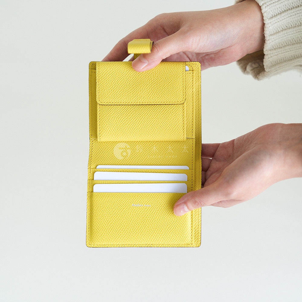 Atelier nuu 亮黃色皮革對折短夾，展示內部多個卡槽和零錢袋，由雙手托住。